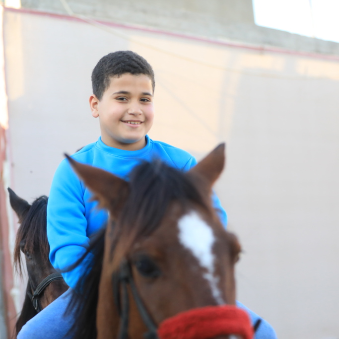 orphan sponsorship in Gaza 2023 - child smiling while horse-riding