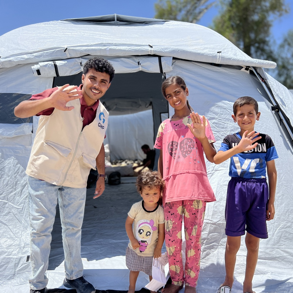 children waving in front of Rahmah camp tent in Gaza