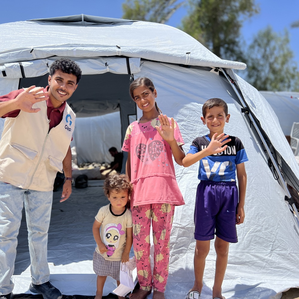 children waving in front of Rahmah camp tent in Gaza